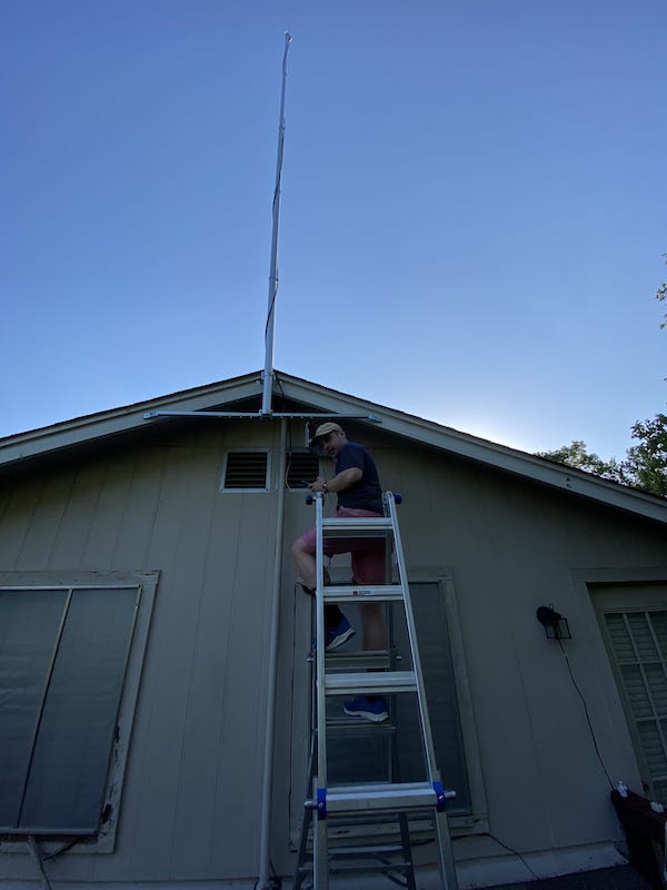 A guy on a ladder mounting a flagpole on his house